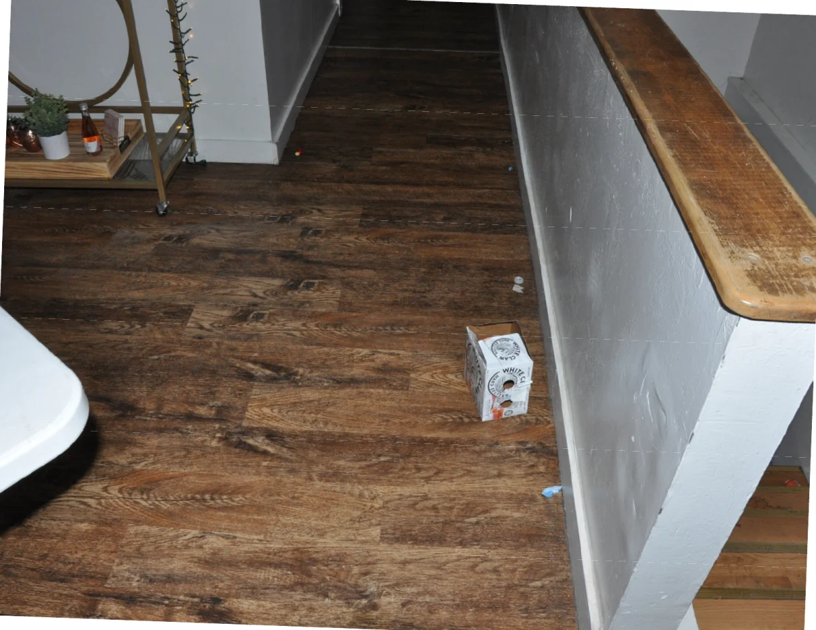 Wood-look floor beside a stair half-wall, with a drink carton near the base.