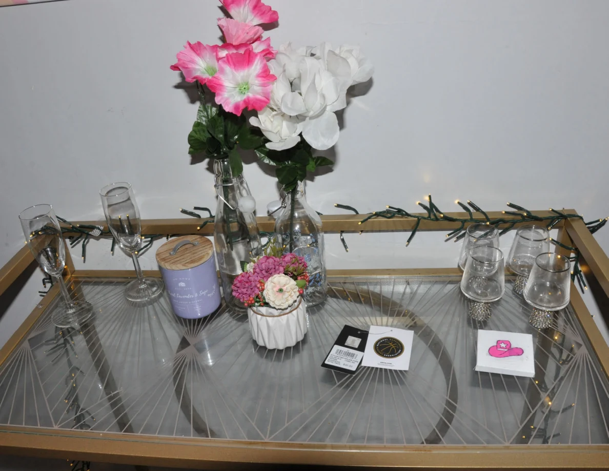Top of a drinks cart with pink and white flowers, candle, glassware and small cards.