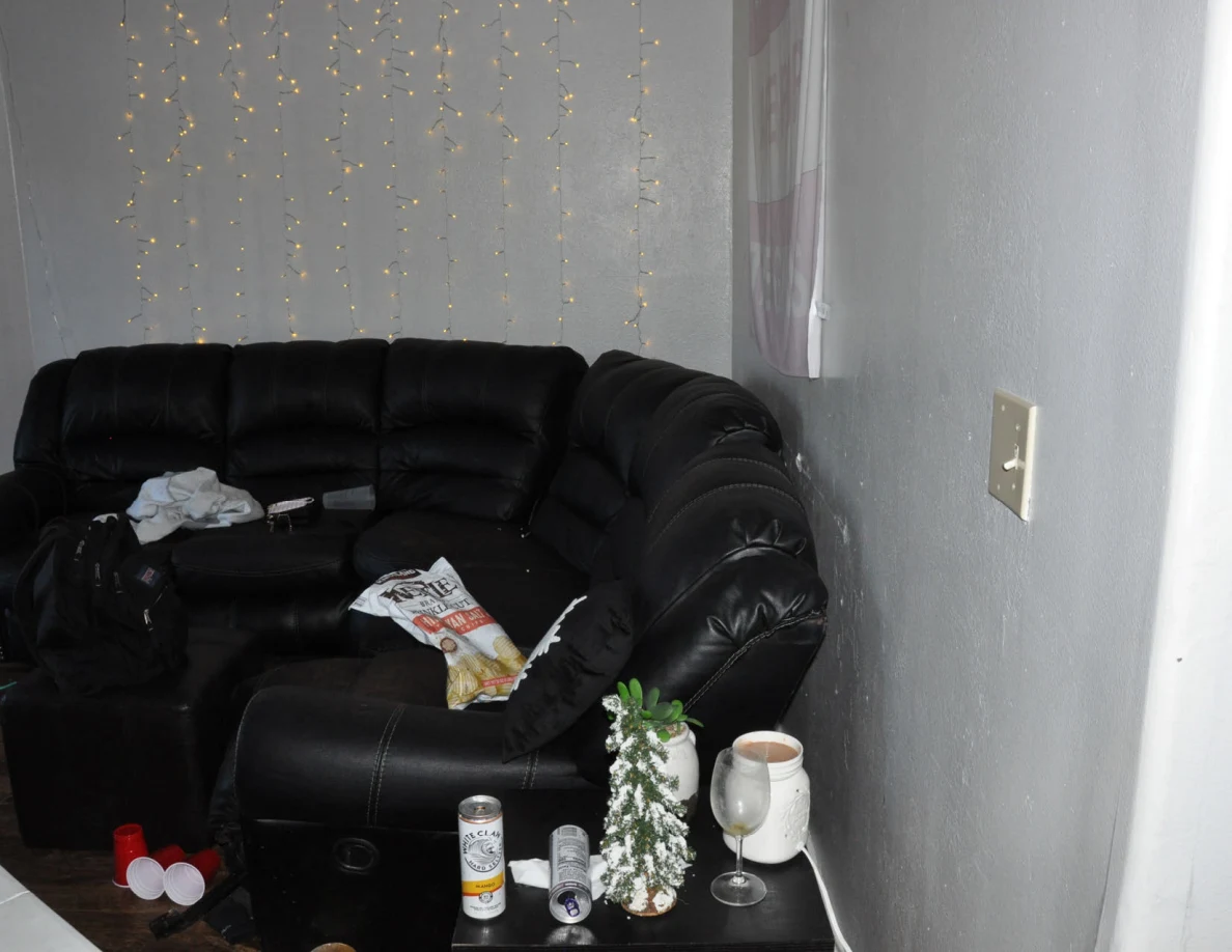 Black sectional sofa beneath string lights with crumpled fabric and packaging on cushions.
