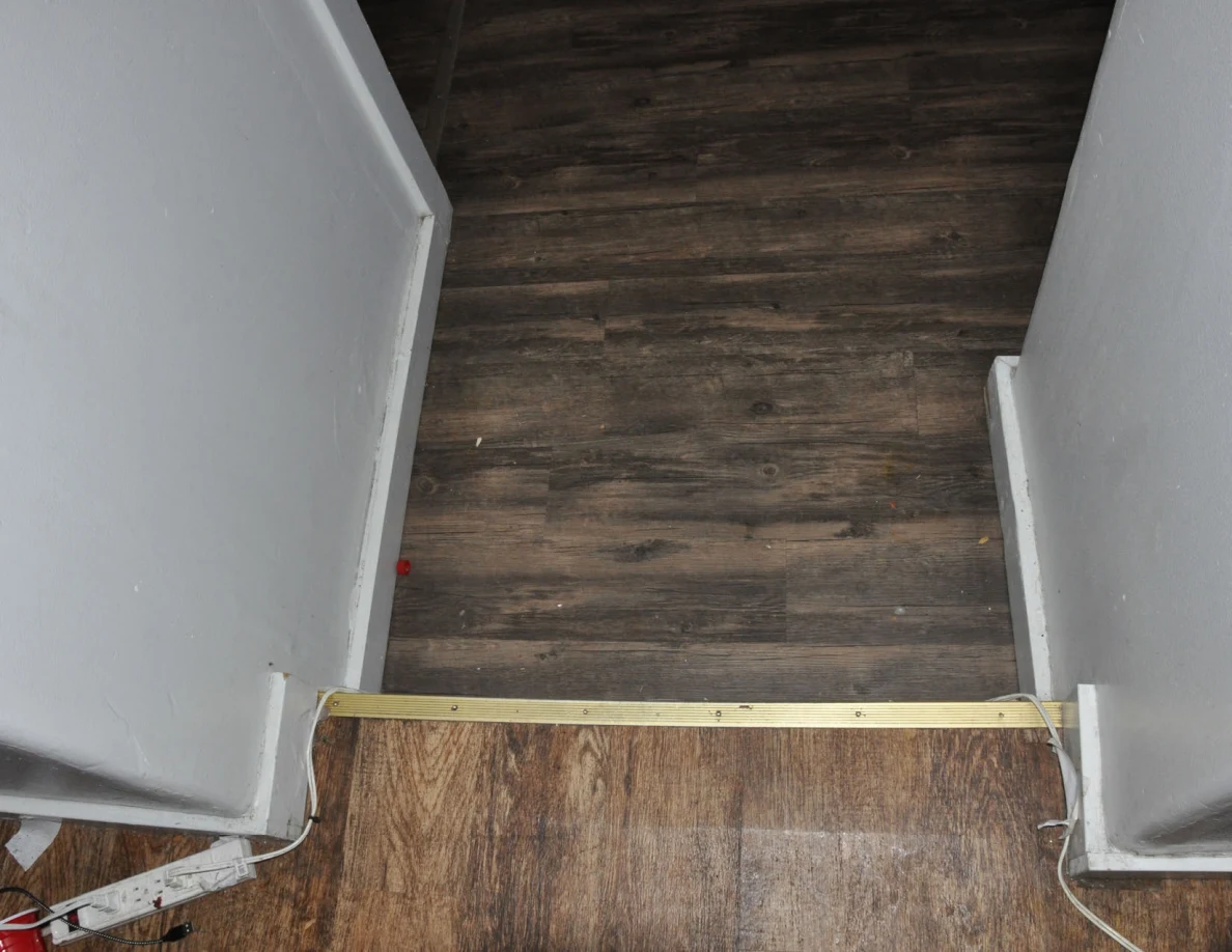 Doorway threshold between two sections of wood-look flooring with a metal transition strip.