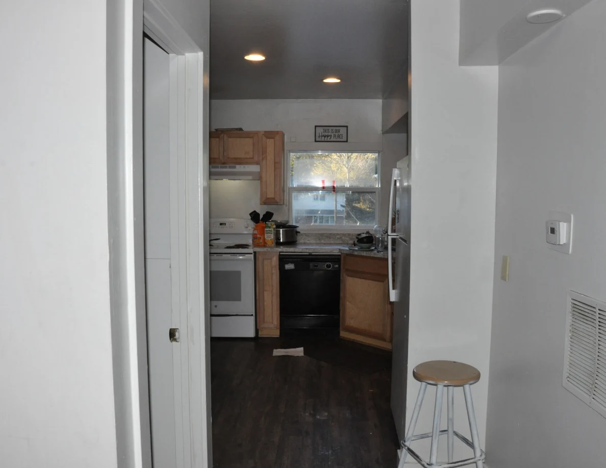 Hallway view into kitchen with stove, dishwasher, wood cabinets and a window.