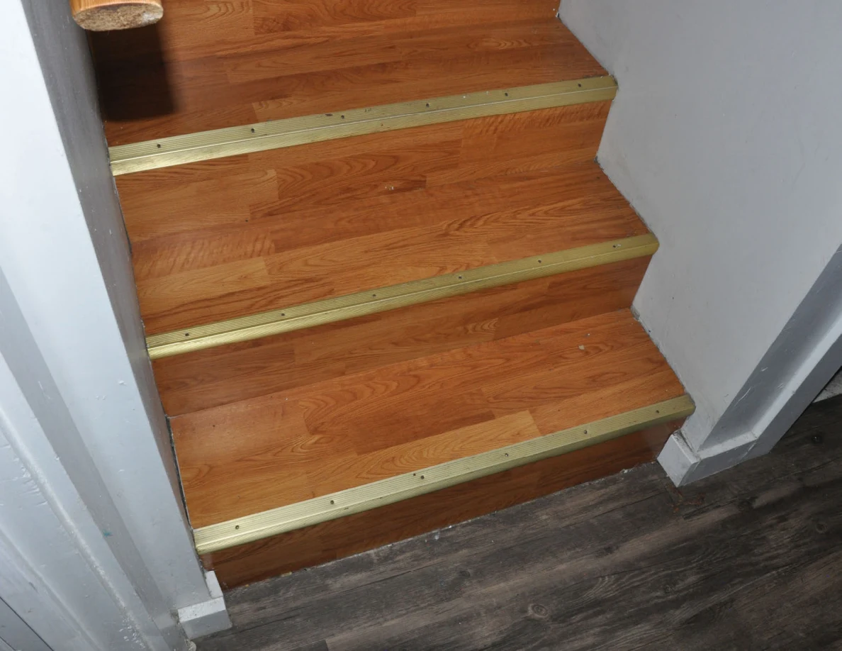 Bottom of a wooden staircase with gold-colored step edges.