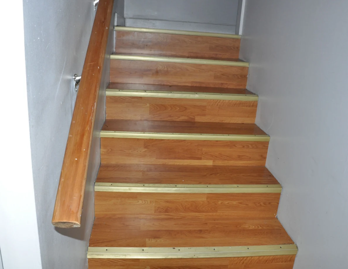 Narrow wooden staircase ascending beside a wooden handrail.
