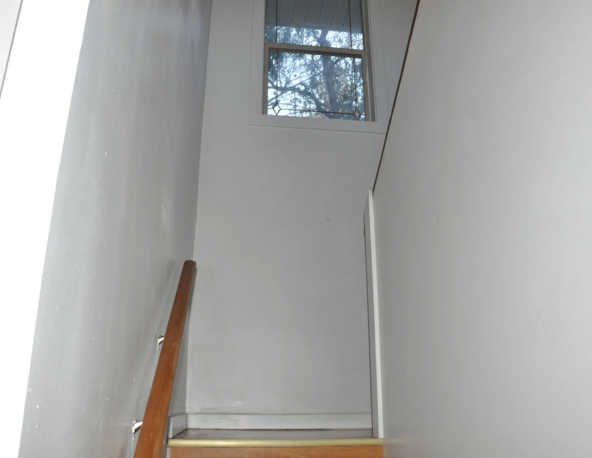 Upper stairwell wall and window above a wooden handrail.
