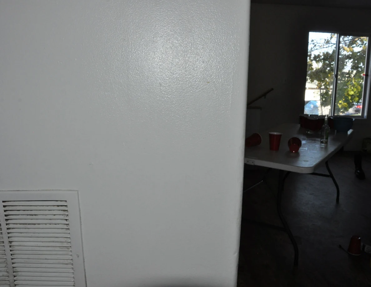 White wall vent beside a doorway with a folding table and red cups visible beyond.