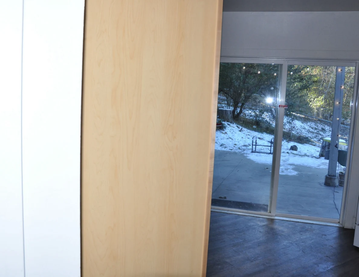 Wooden door partly framing a sliding glass door and snow-covered patio beyond.