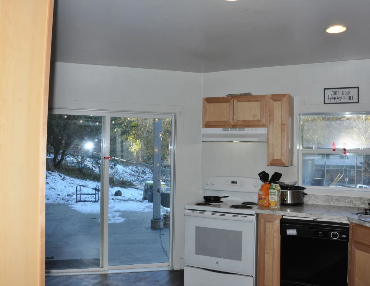 Kitchen with wood cabinets, white stove, black dishwasher and sliding glass door overlooking snow.