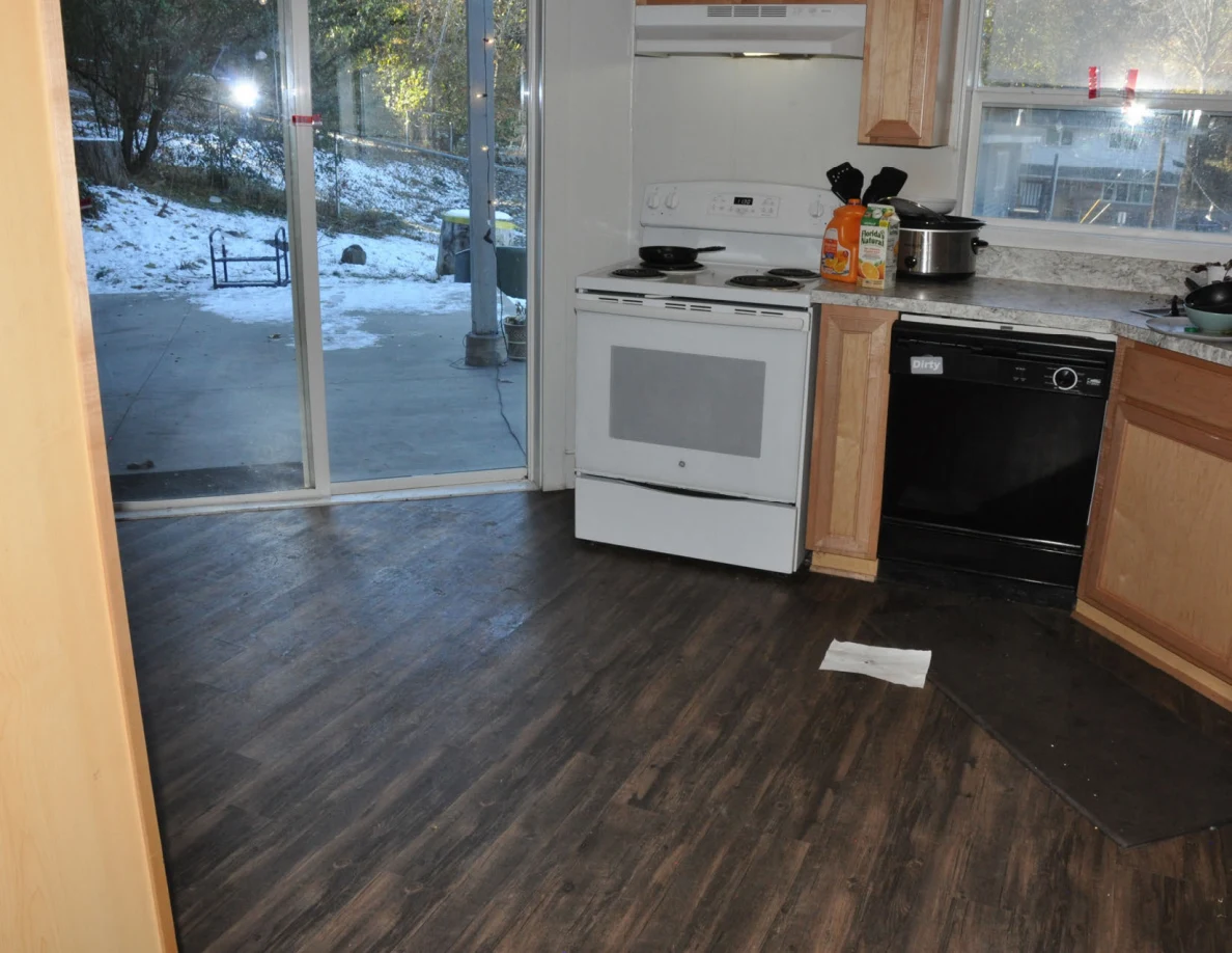 Kitchen floor below a white stove and black dishwasher, beside a sliding glass door.