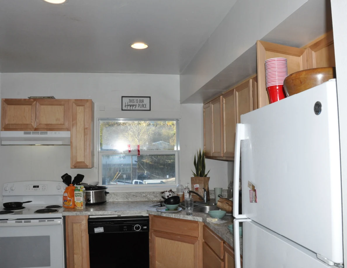 Kitchen overview with white refrigerator, stove, black dishwasher, wood cabinets and countertop items.