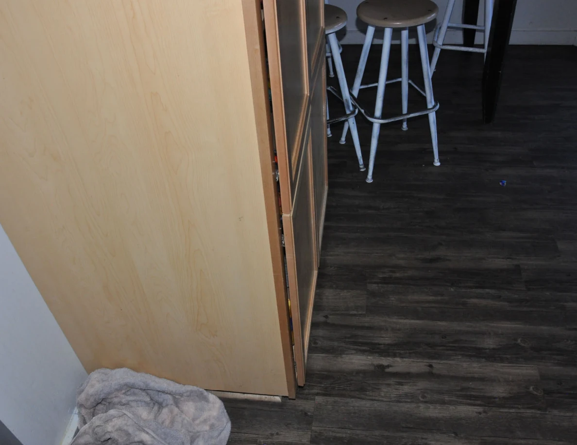 View beside a wooden door toward kitchen stools, with gray cloth on the floor.
