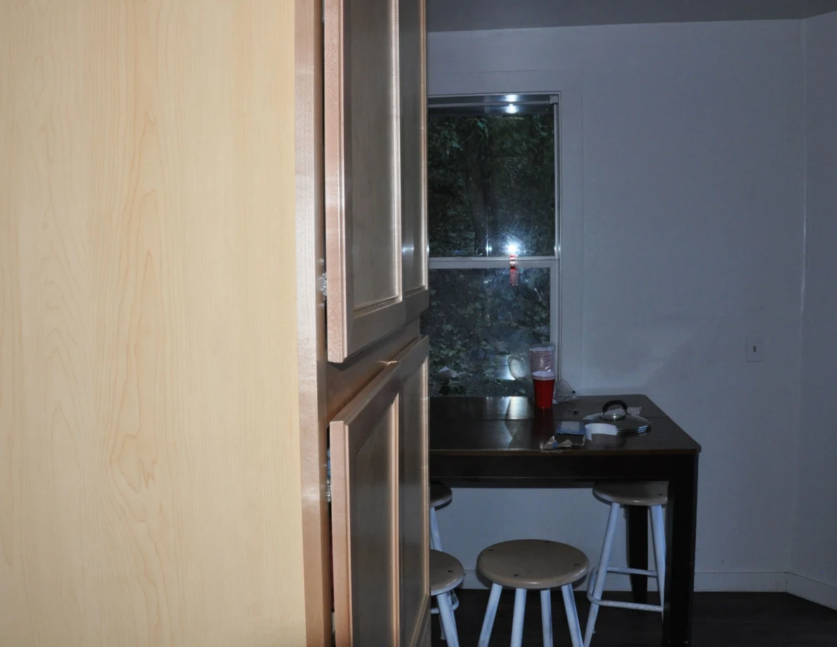 Wooden cabinet edge framing a table, stools and window in a kitchen corner.