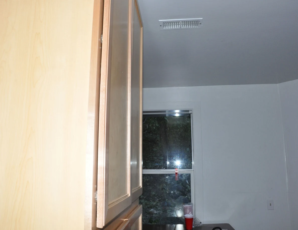 Upper wooden cabinet edge beside a kitchen ceiling vent and window.
