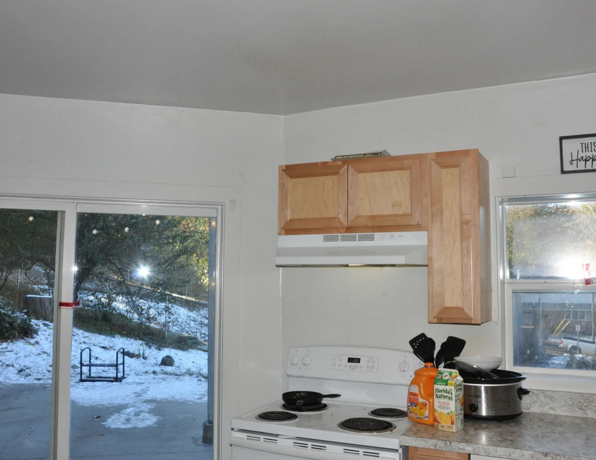 White stove below a wooden cabinet and range hood beside a sliding glass door.