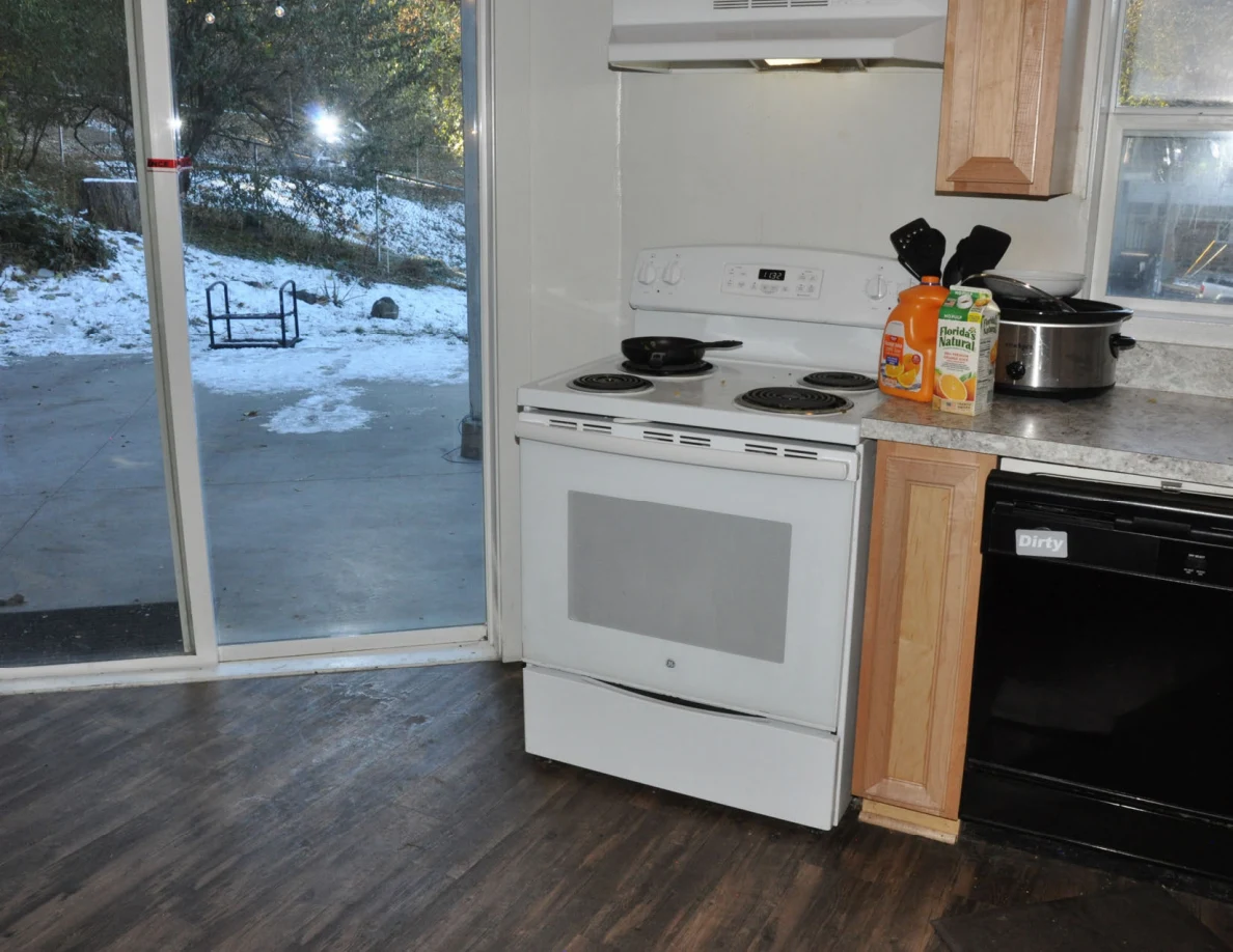 White electric stove and black dishwasher beside a counter holding juice containers and a slow cooker.