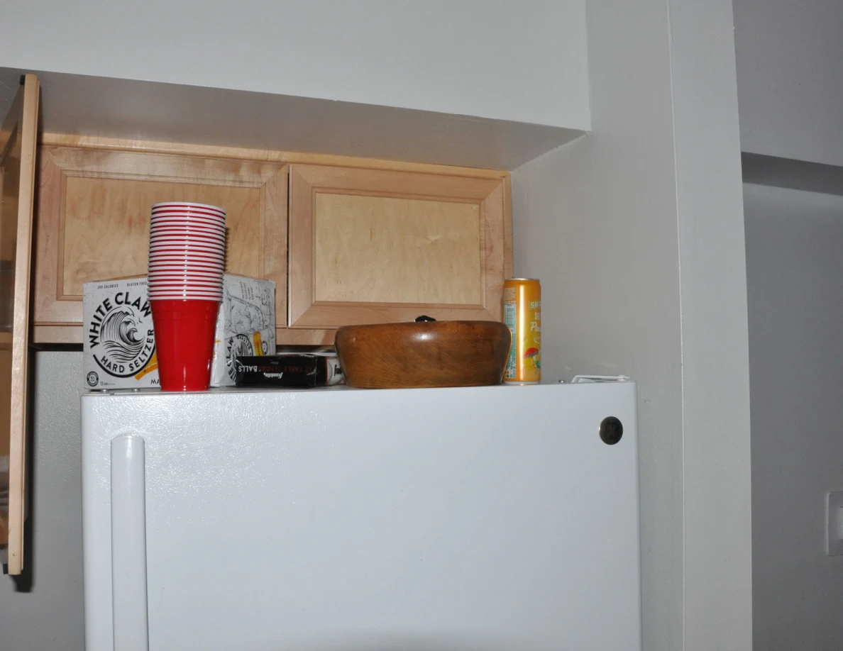 Top of refrigerator with stacked red cups, a wooden bowl, carton and tall container.