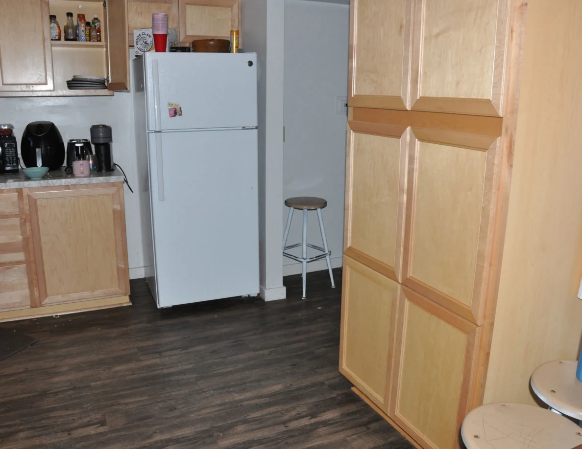 Kitchen refrigerator and tall wooden pantry cabinet with a stool in the doorway.
