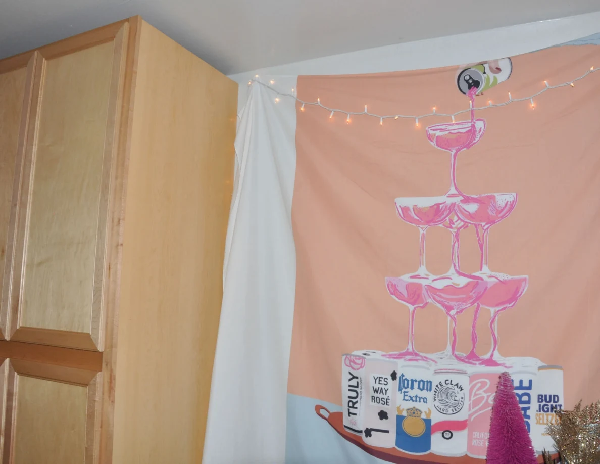 Colorful drinks-themed wall hanging with string lights beside a tall wooden cabinet.