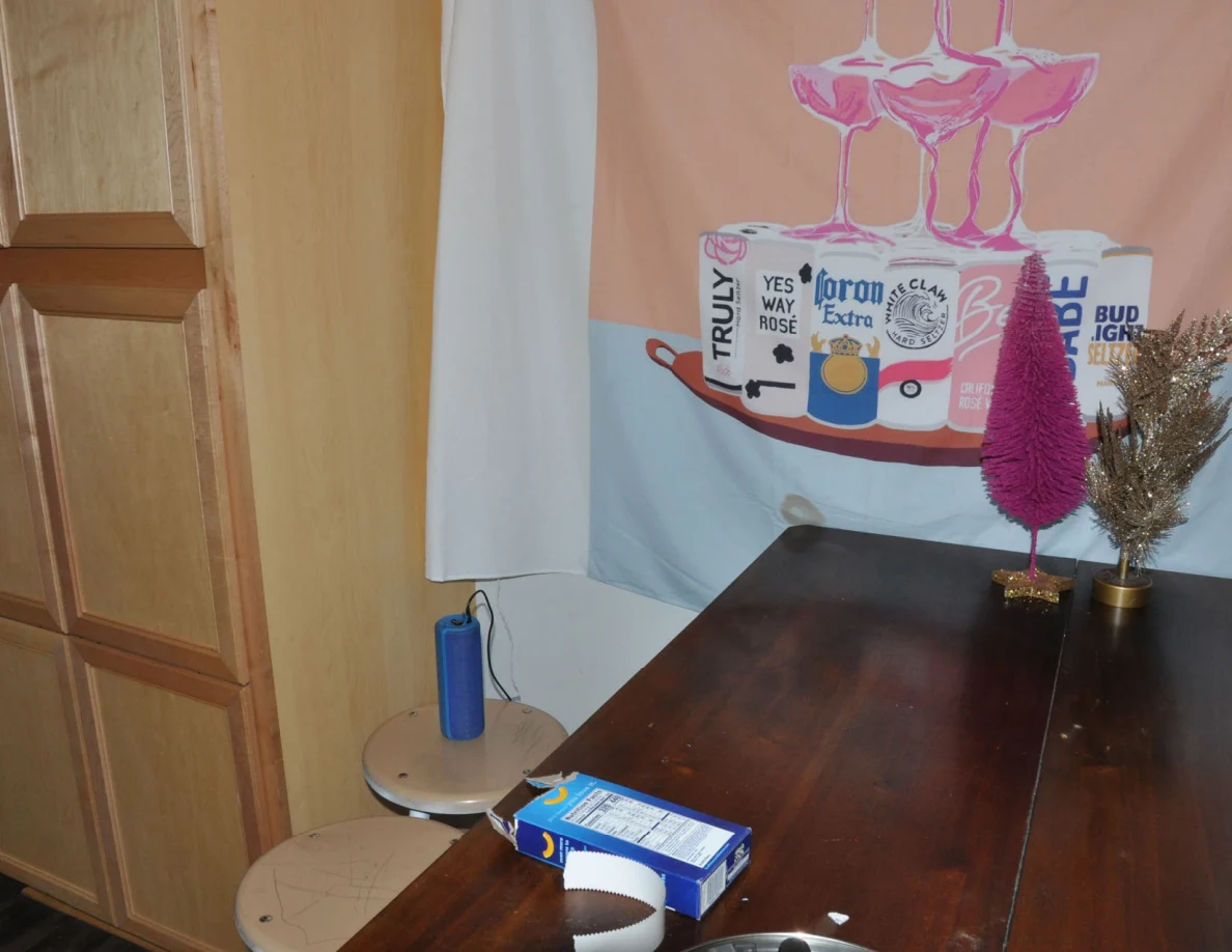 Kitchen table and stools below a drinks-themed wall hanging, with small decorative trees and blue speaker nearby.