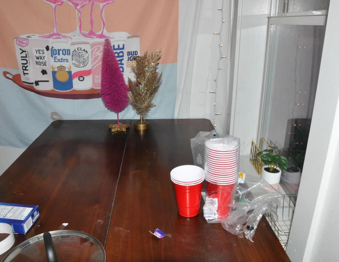 Wooden table with small pink and gold decorative trees, stacked red cups and plastic wrapping.
