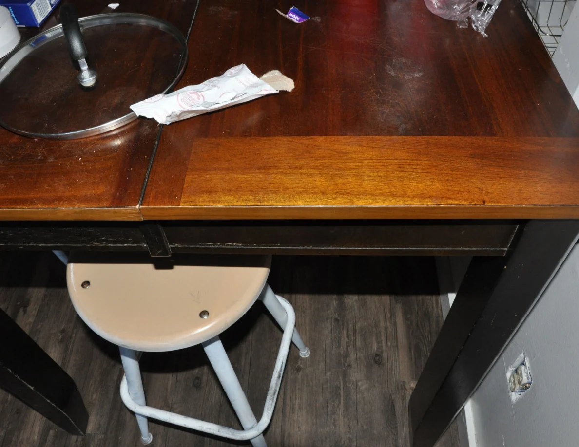 Wooden table edge with a glass pot lid and paper towel above a stool.
