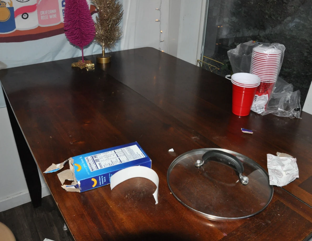 Kitchen table holding a glass lid, opened carton, paper towel and stacked red cups.