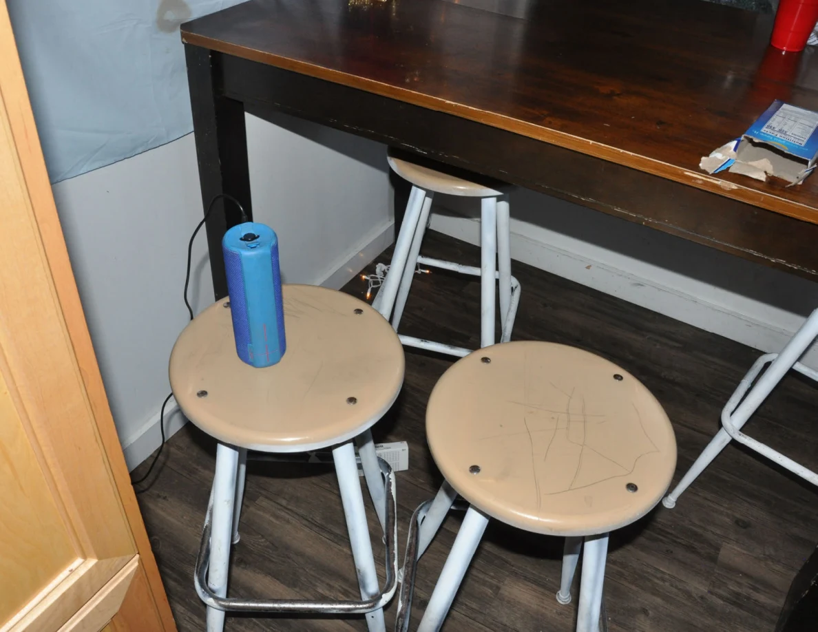 Blue cylindrical speaker standing on one of several stools beside a kitchen table.
