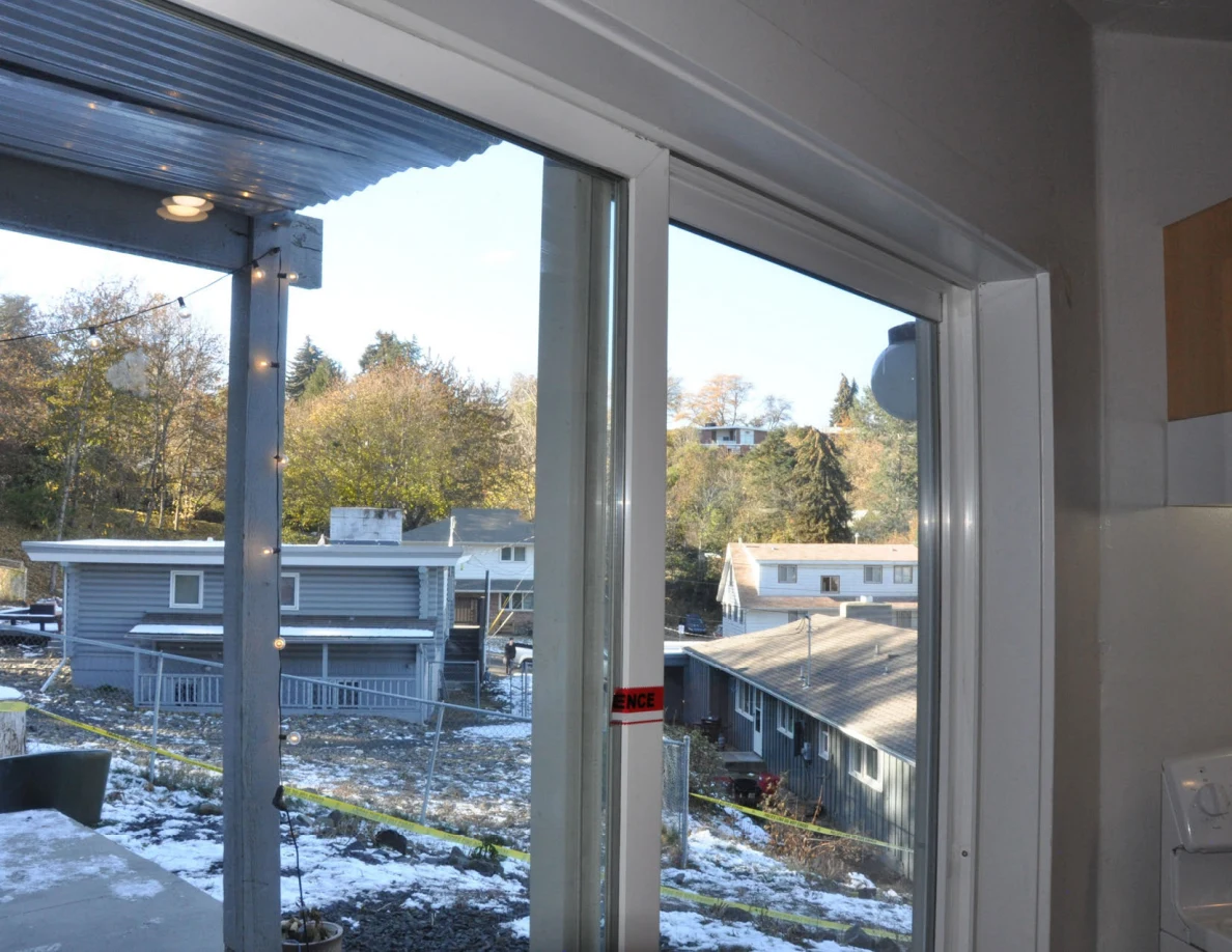Sliding glass doors overlooking a snowy slope and neighboring houses.