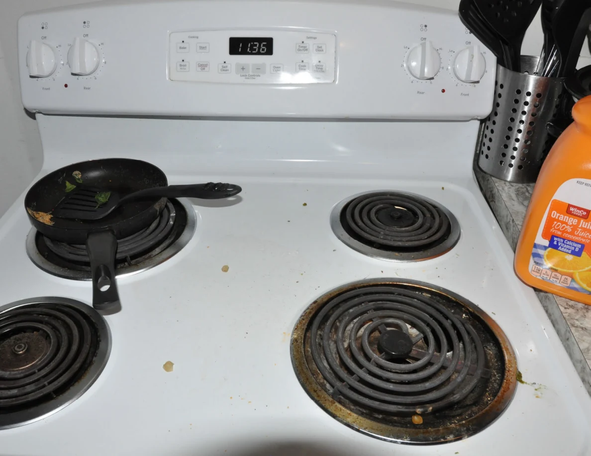 White electric stovetop with a small frying pan, utensils and crumbs around coil burners.