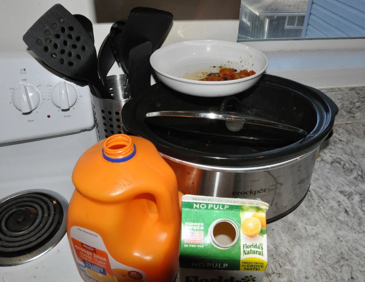 Slow cooker and bowl beside orange juice containers and a utensil holder.