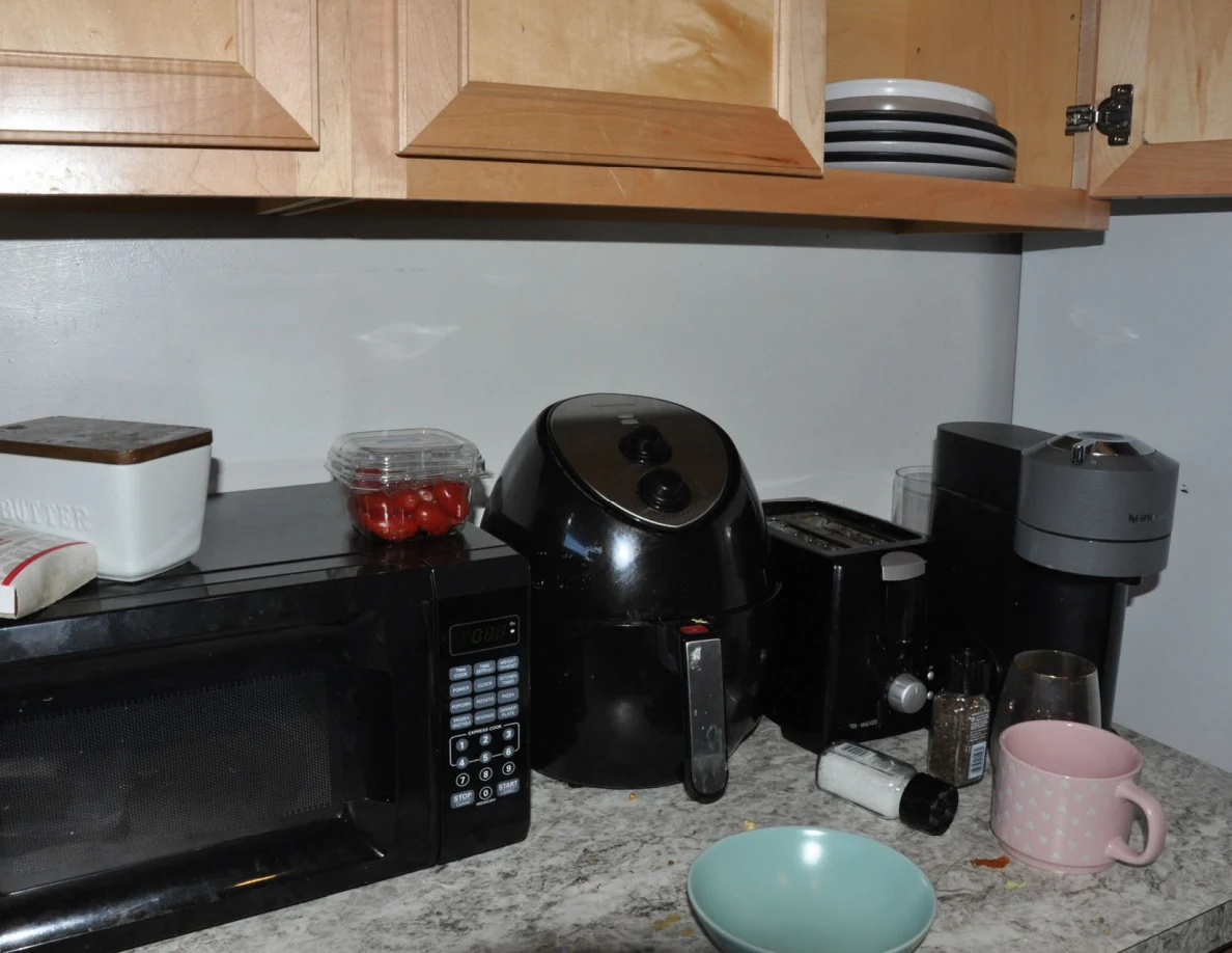 Kitchen counter with microwave, air fryer, coffee maker, pink mug and turquoise bowl.