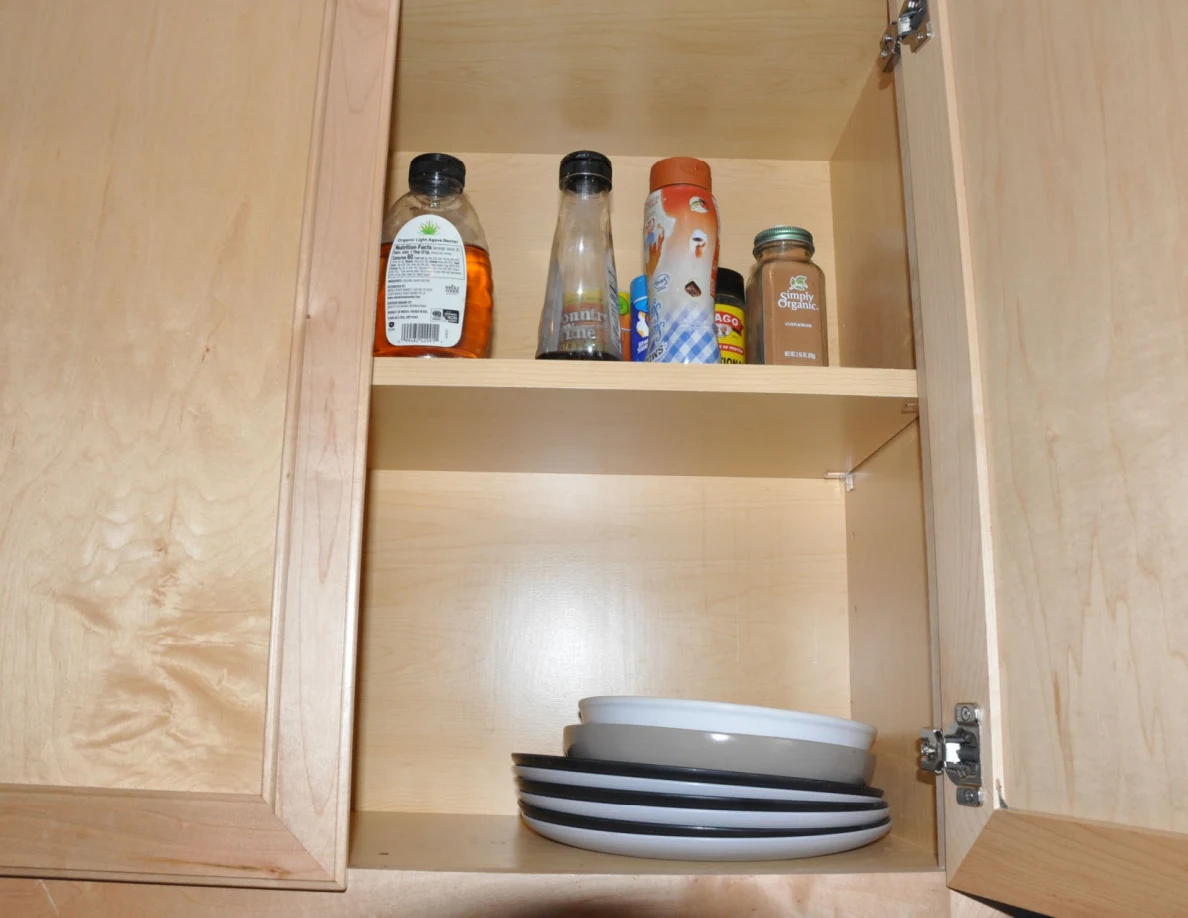 Open wooden cabinet with condiment bottles above stacked plates and bowls.