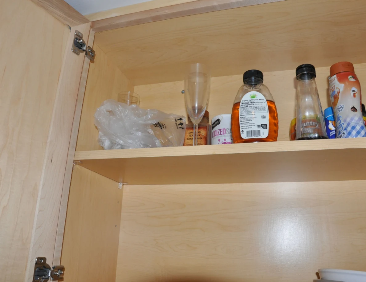 Upper cabinet shelf holding condiment bottles, a glass and plastic packaging.