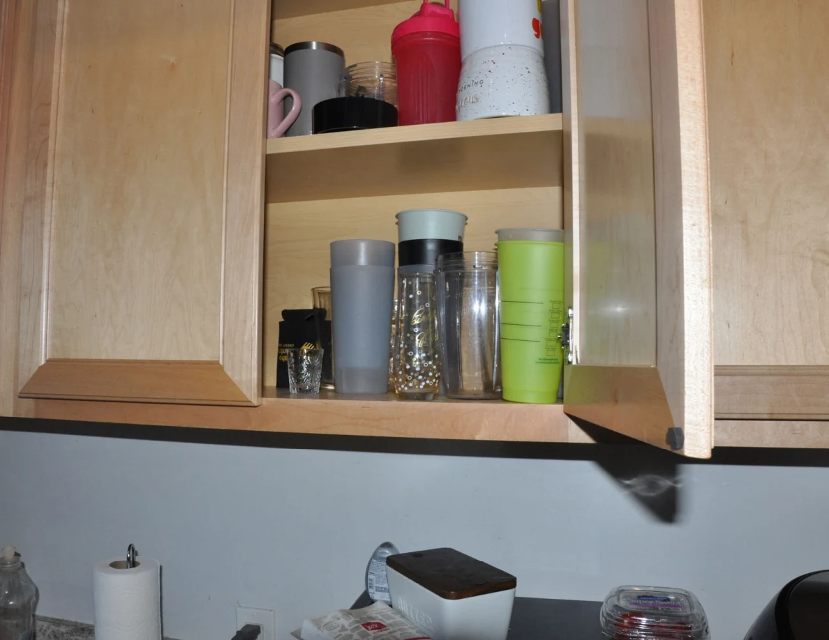Open kitchen cabinet filled with mugs, tumblers and drinking glasses.