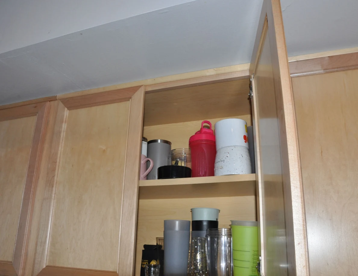Upper kitchen cabinet with colorful mugs, shaker bottle and tall cups.