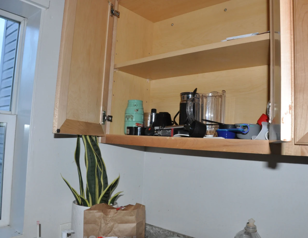 Open cabinet with mostly empty upper shelves and cups, pitchers and utensils below.