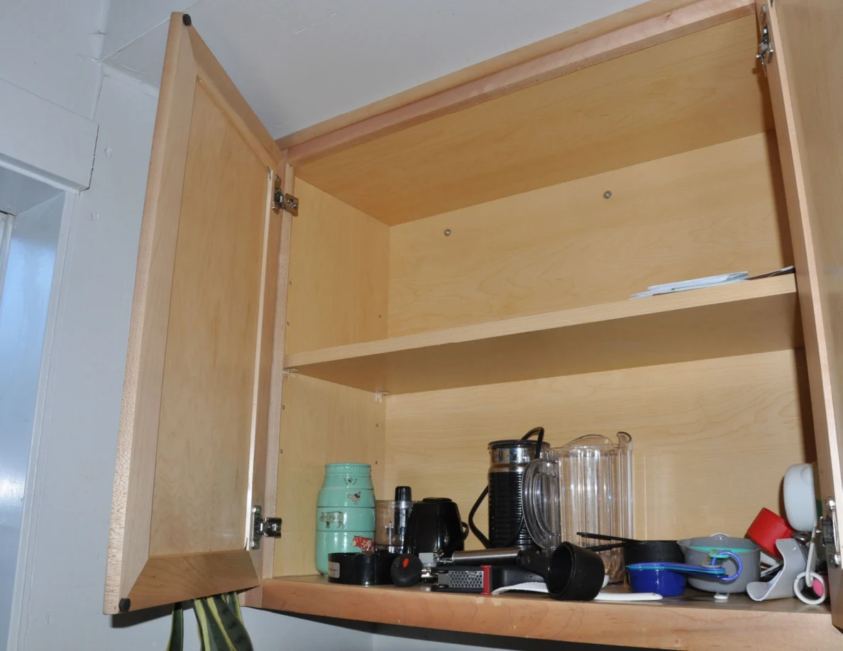 Cabinet lower shelf with glass pitchers, mugs and assorted small kitchen items.