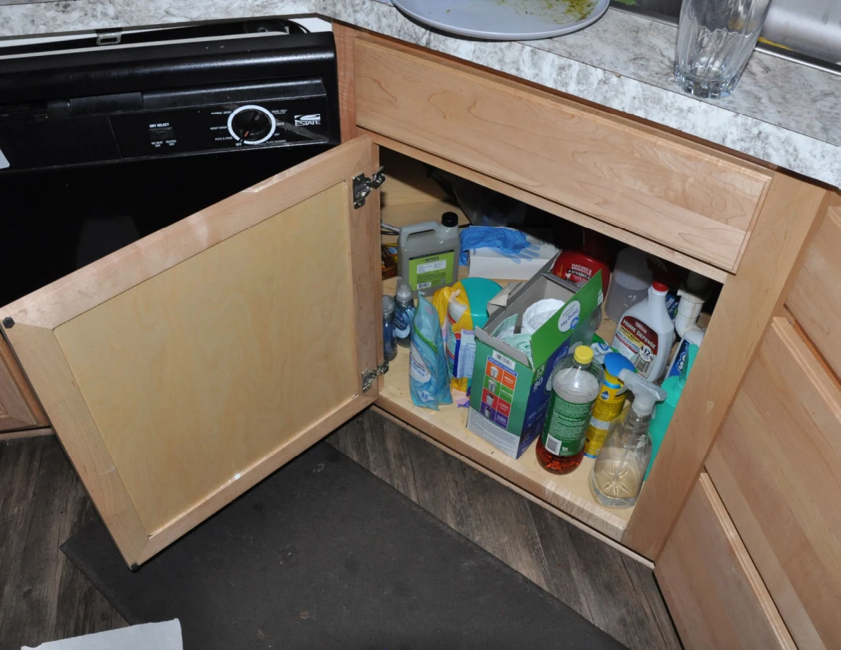 Open cabinet beneath kitchen sink filled with cleaning bottles and supplies.