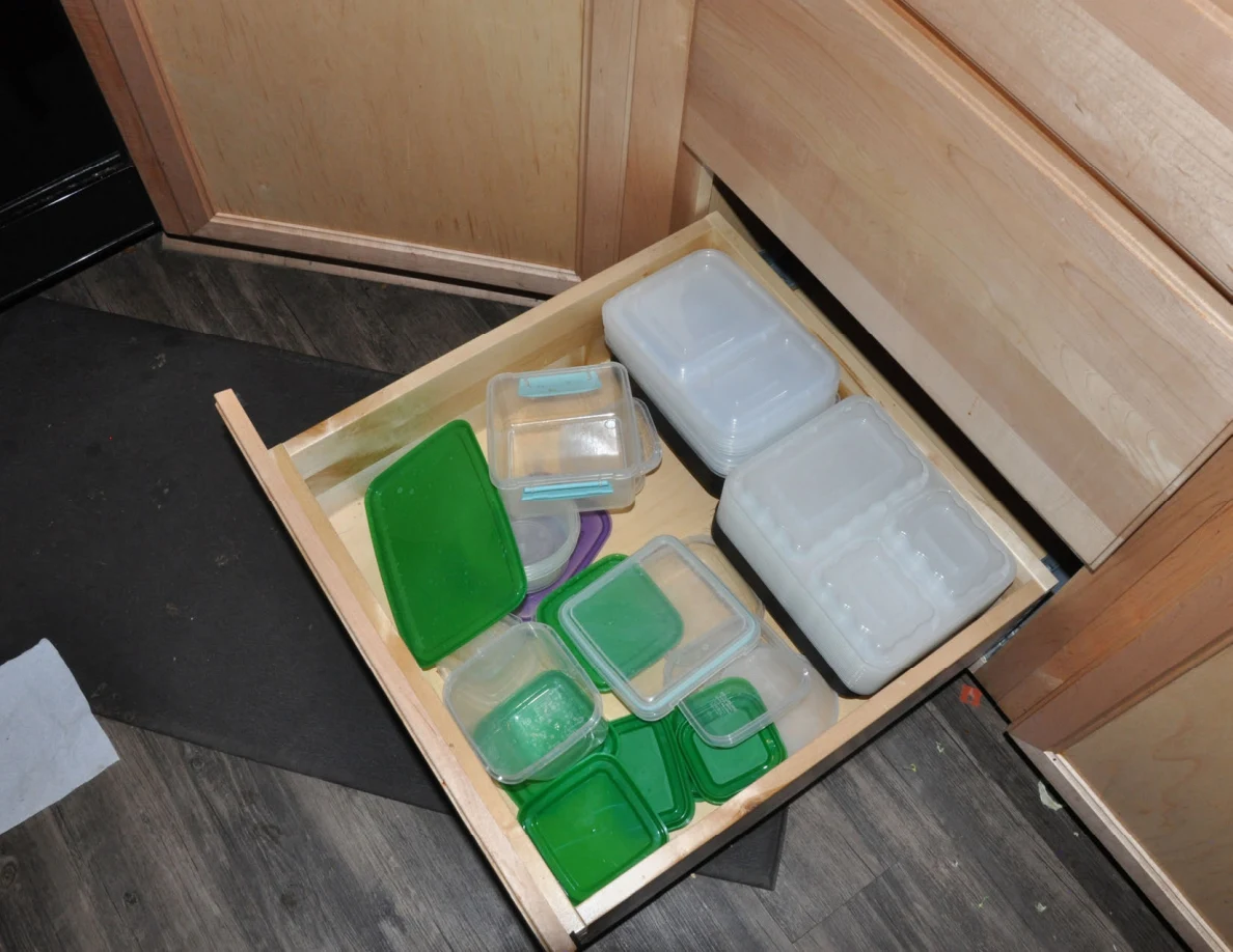 Open kitchen drawer with plastic food-storage containers and green lids.