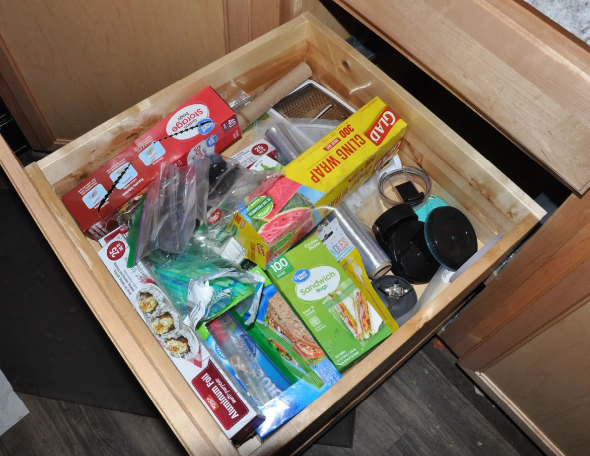 Open drawer holding plastic wrap, food-storage bags, packaged snacks and small kitchen items.