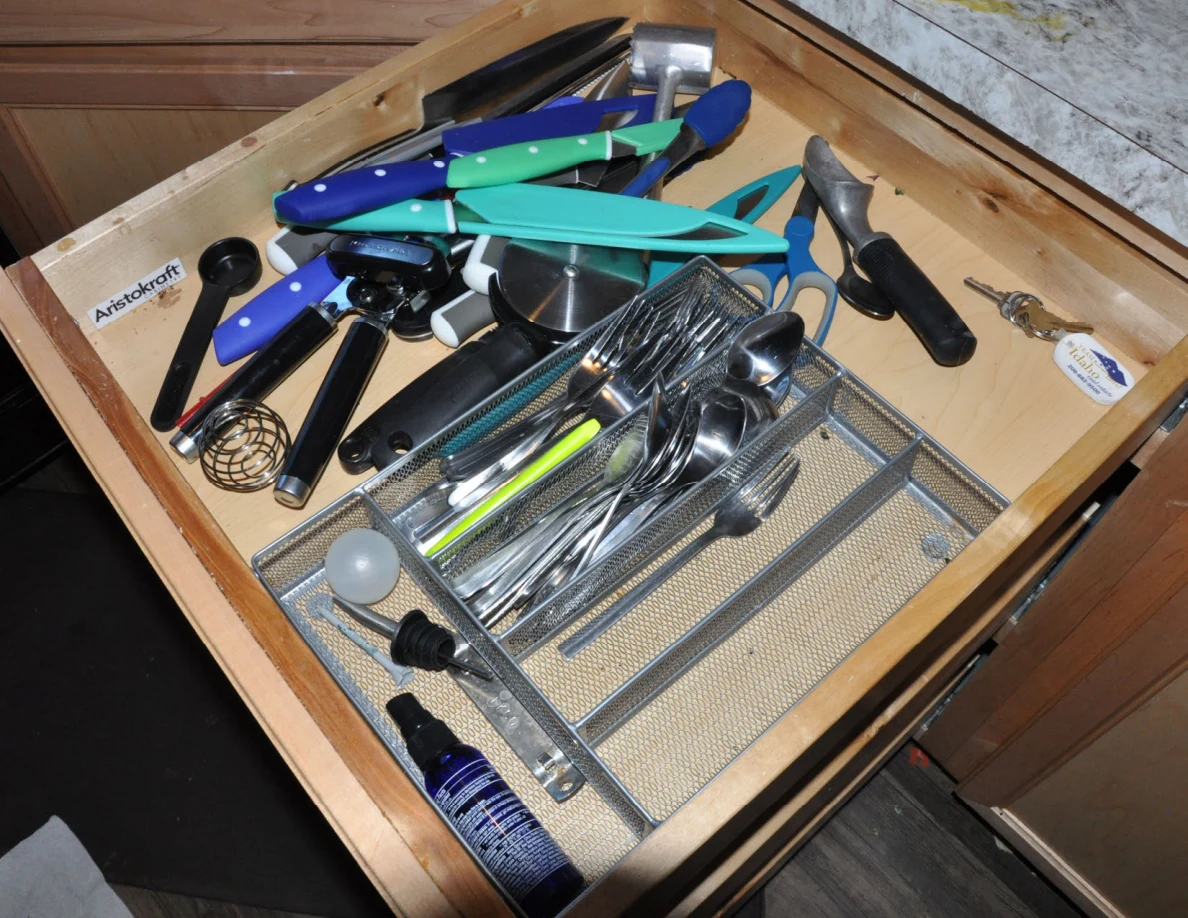 Cutlery drawer with forks, spoons, knives, whisks and colorful-handled kitchen utensils.