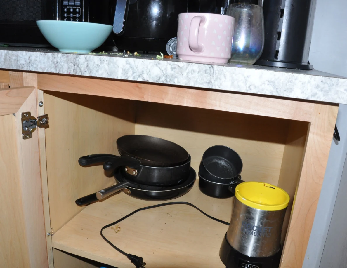 Open lower cabinet with stacked pots and a small electric appliance below counter mugs.