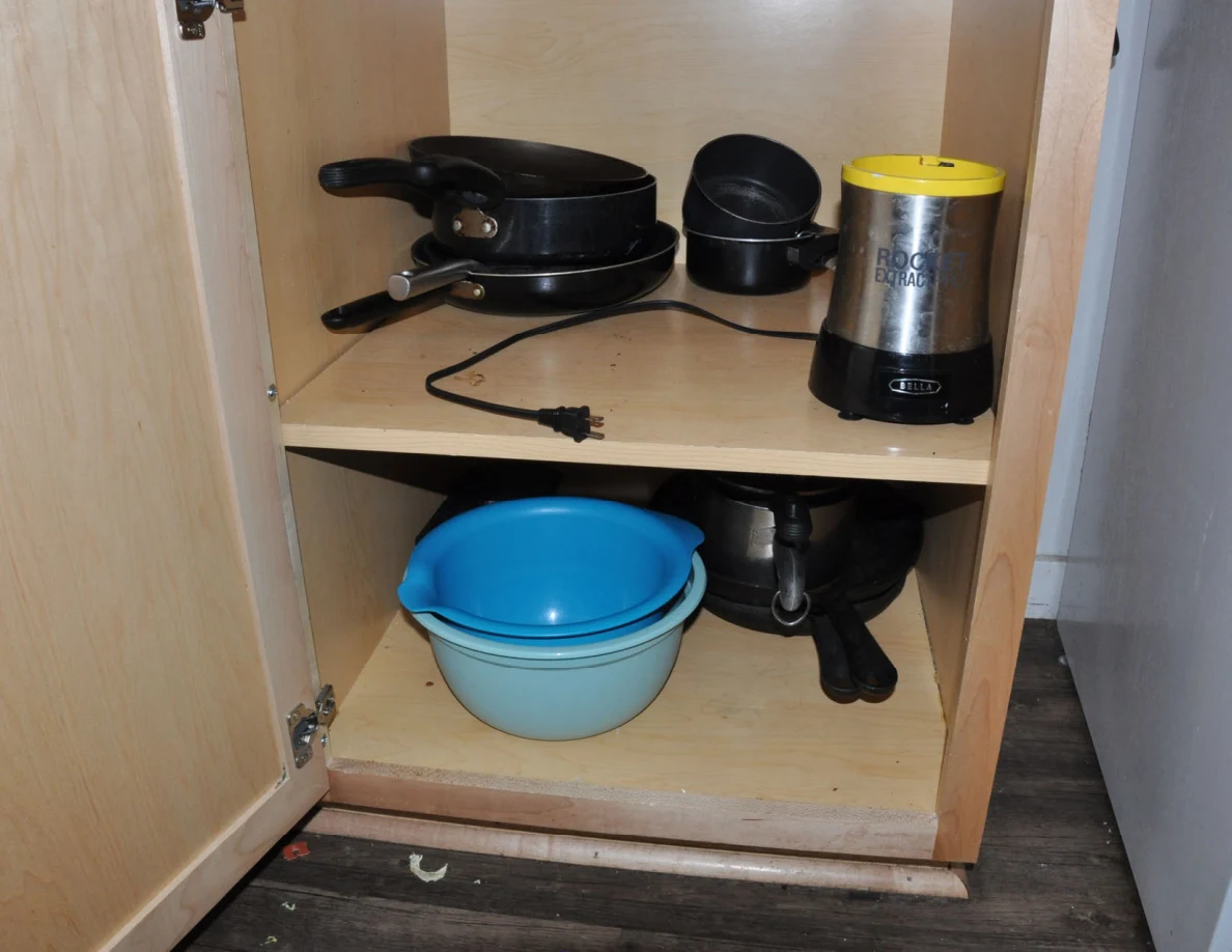 Lower kitchen cabinet with pots, mixing bowls and a small yellow-topped appliance.