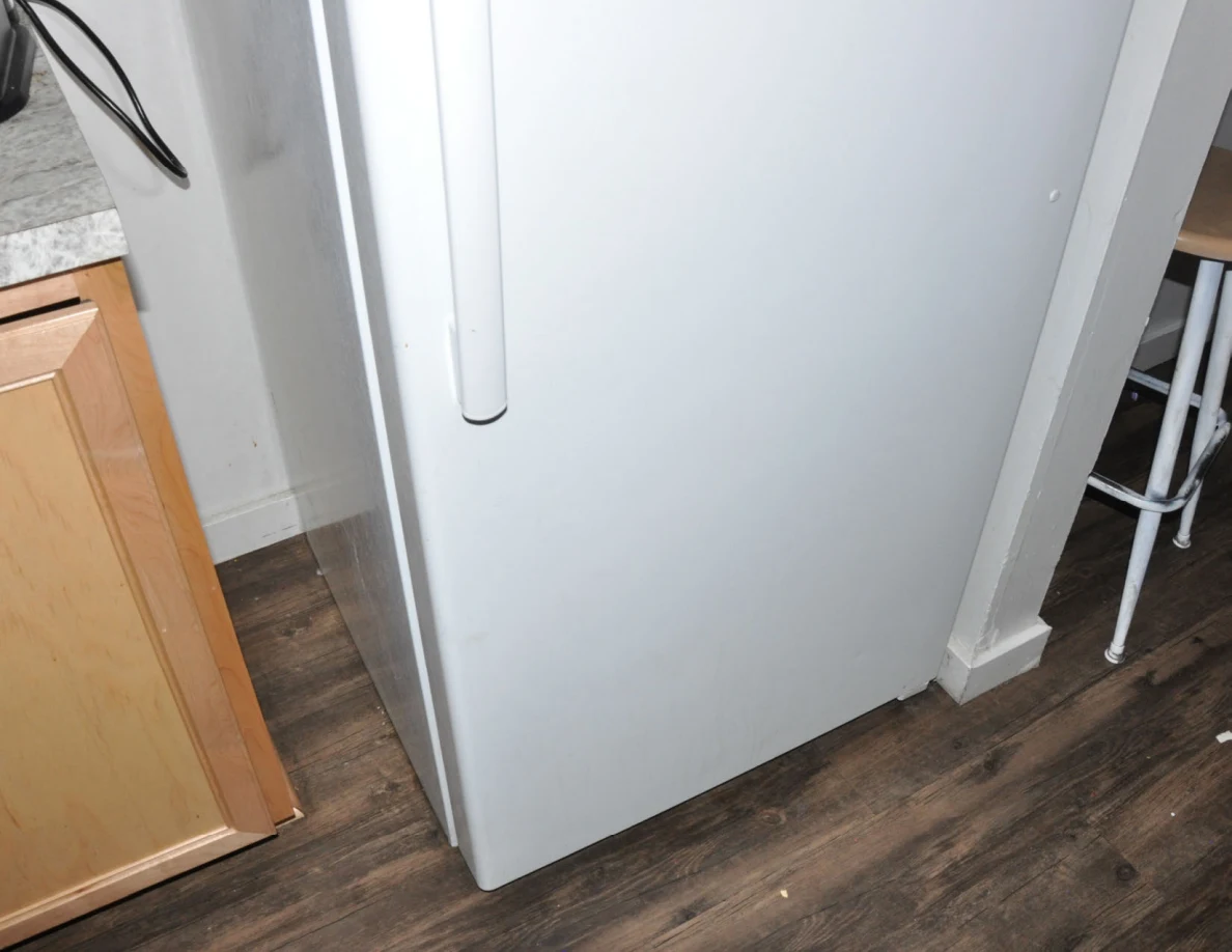 Closed white refrigerator door and handle beside wooden kitchen cabinets.