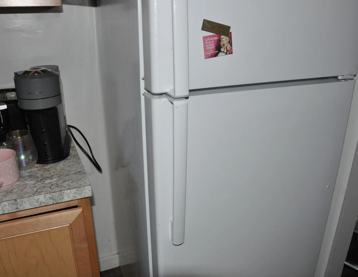 Closed white refrigerator and freezer with a small card attached to the upper door.