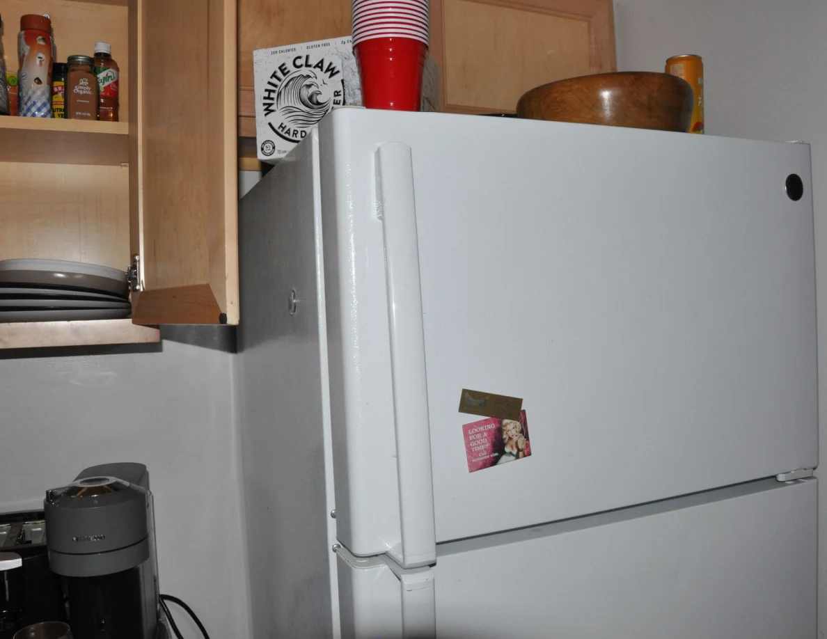 Upper white refrigerator with stacked cups, bowl and carton on top.