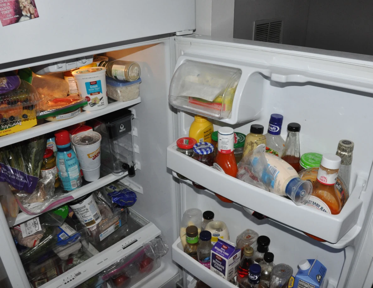 Open refrigerator filled with food containers, vegetables and condiments.