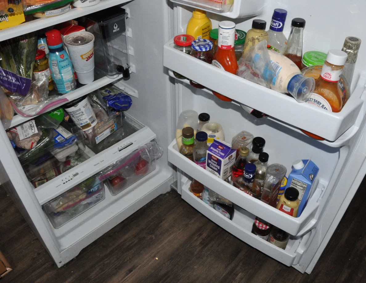 Refrigerator door shelves packed with bottles and jars beside shelves of food.