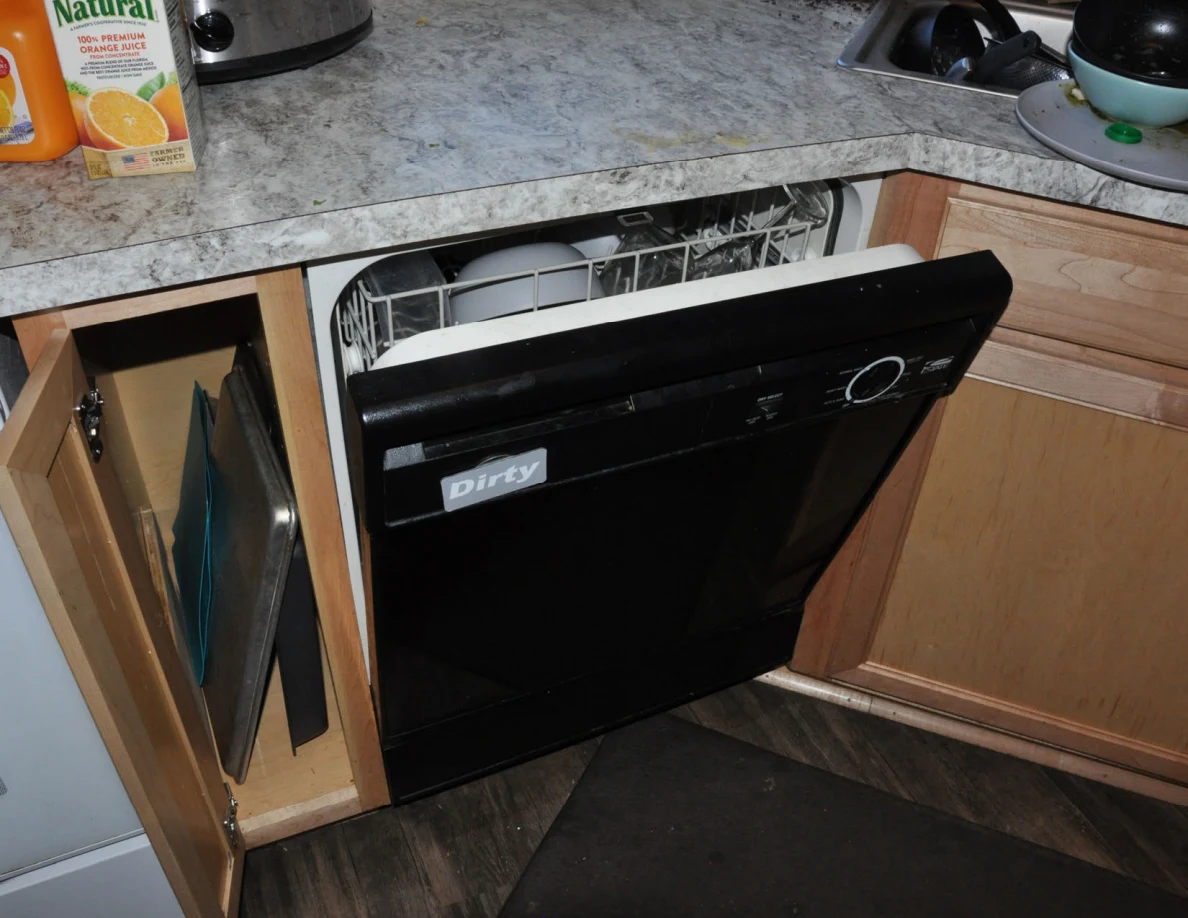 Partly open black dishwasher with a Dirty label beneath a kitchen counter.