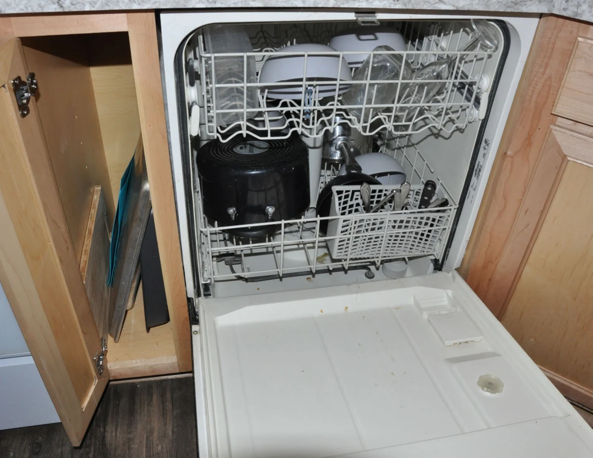 Open dishwasher containing pots, bowls, glasses and cutlery.
