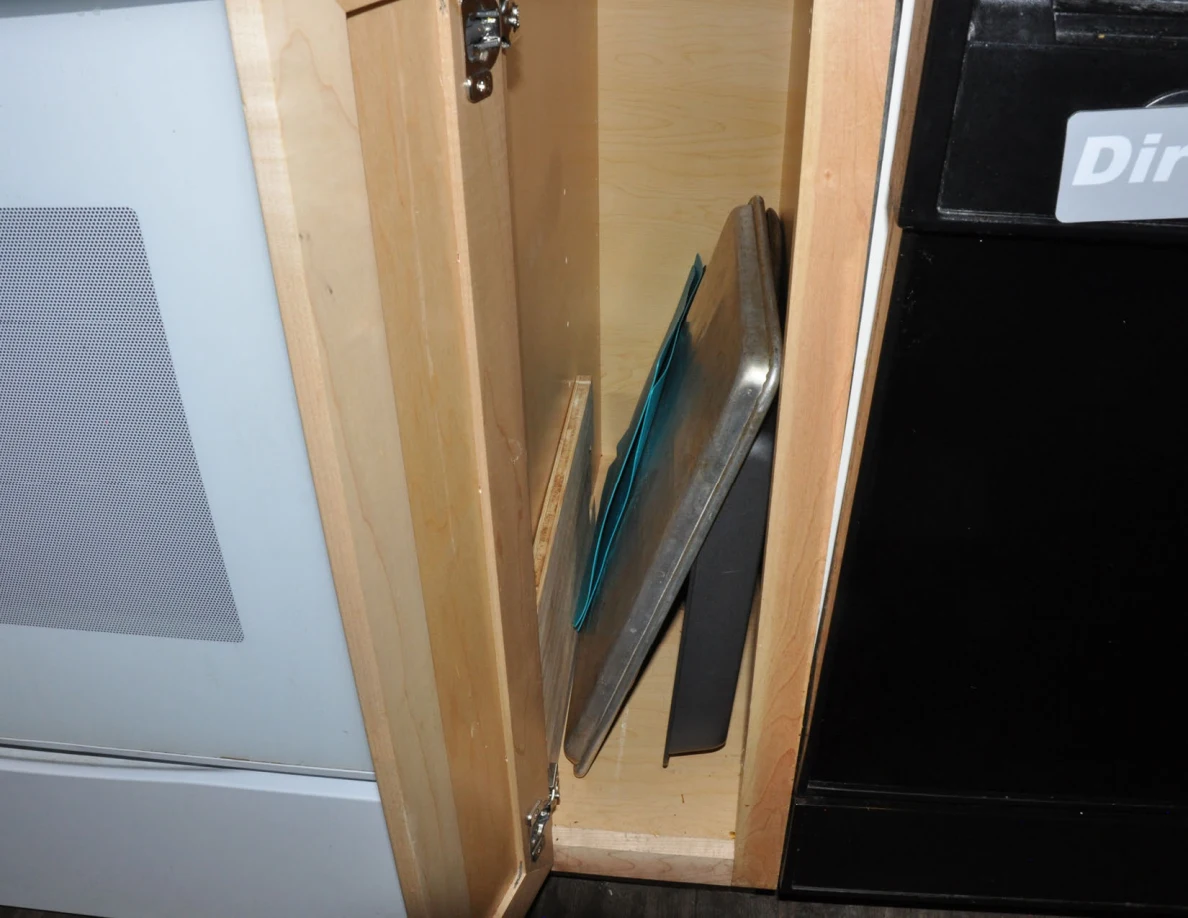 Narrow kitchen cabinet storing baking trays and boards upright beside the dishwasher.